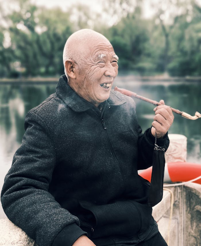 Senior man smoking a pipe by a lake, evoking calm and serenity outdoors.