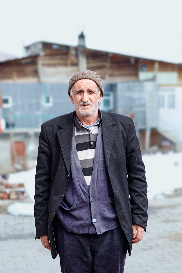Elderly man standing outdoors in winter, wearing warm clothing and a beanie.